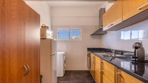 A compact kitchen with wooden cabinets, a built-in oven, and a window above the sink. - Monumental Apartment 712 Balcony Sea View (Funchal)