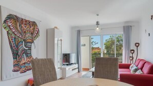 A living room with a round table, two chairs, a red sofa, a TV, and a large elephant artwork on the wall. - Alta do Garajau II 2 AT (Santa Cruz)