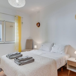A hotel room with a bed, a bedside table, a lamp, a mirror, and a window with curtains. - Alta do Garajau II 2 AT (Santa Cruz)