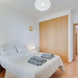 A bedroom with a bed, a wooden wardrobe, and a bedside lamp. - Alta do Garajau II 2 AT (Santa Cruz)