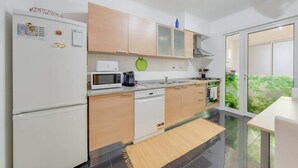 A modern kitchen with white appliances, wooden cabinets, and a view of greenery through the window. - Alta do Garajau II 2 AT (Santa Cruz)