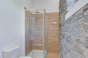 Une salle de bain avec une douche à parois de verre, des toilettes et un mur en pierre.