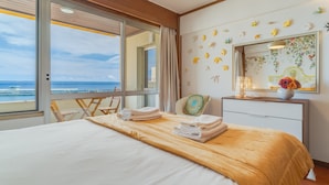 Une chambre d’hôtel avec un lit, une chaise, une commode et une grande fenêtre donnant sur la mer.