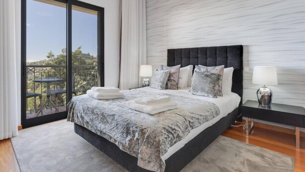Een moderne slaapkamer met een groot bed, twee nachtkastjes en een balkon met een tafel en stoelen.
