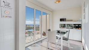 A modern kitchen with white cabinets and a dining area with a glass table and chairs. - Anje Apartamento 4 Q (Funchal)