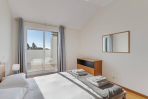 A hotel room with a bed, a nightstand, a wooden dresser, a mirror, and a sliding glass door leading to a balcony. - Anje Apartamento 4 Q (Funchal)