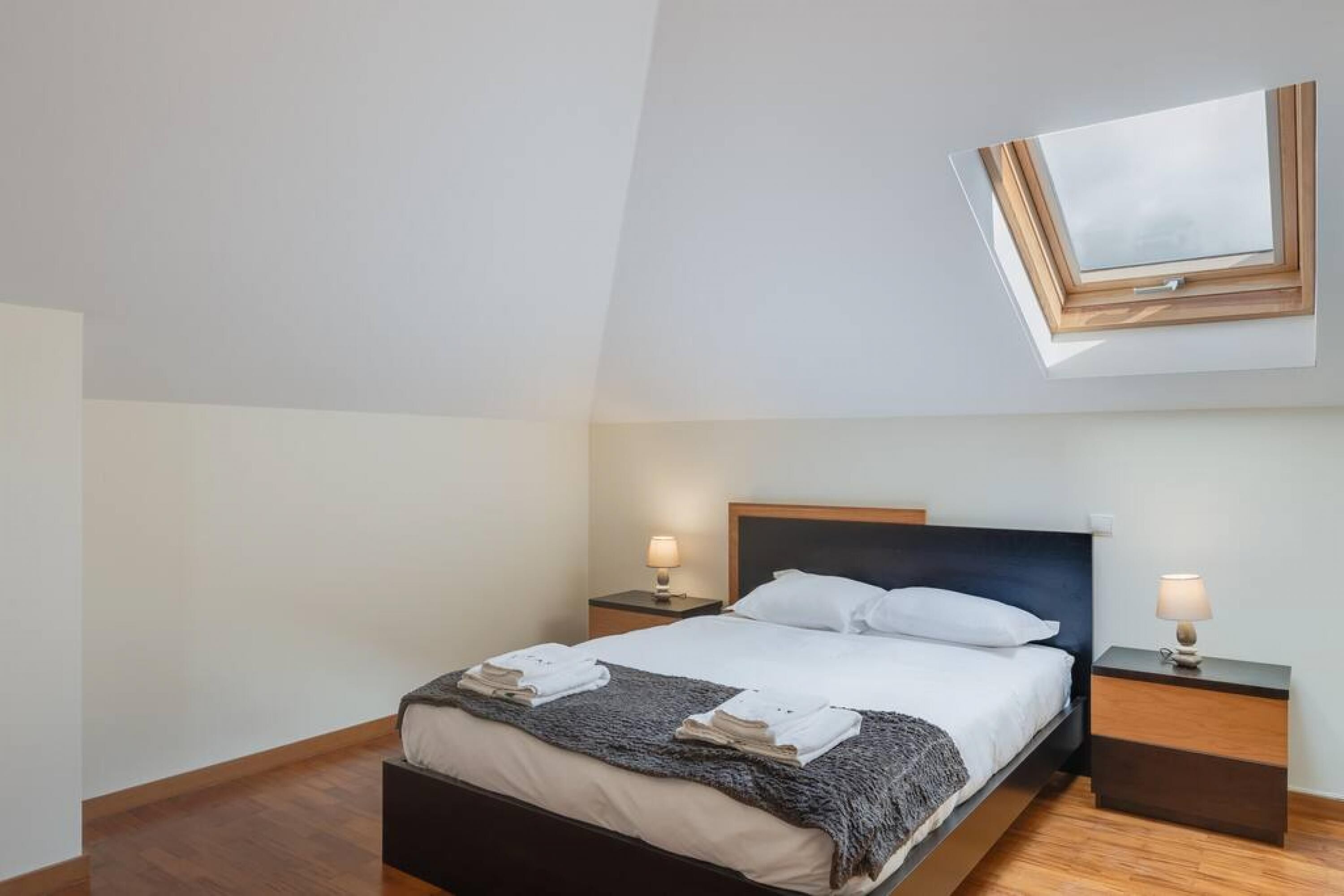 A modern hotel room with a skylight, a bed with neatly folded towels, and two bedside tables with lamps.