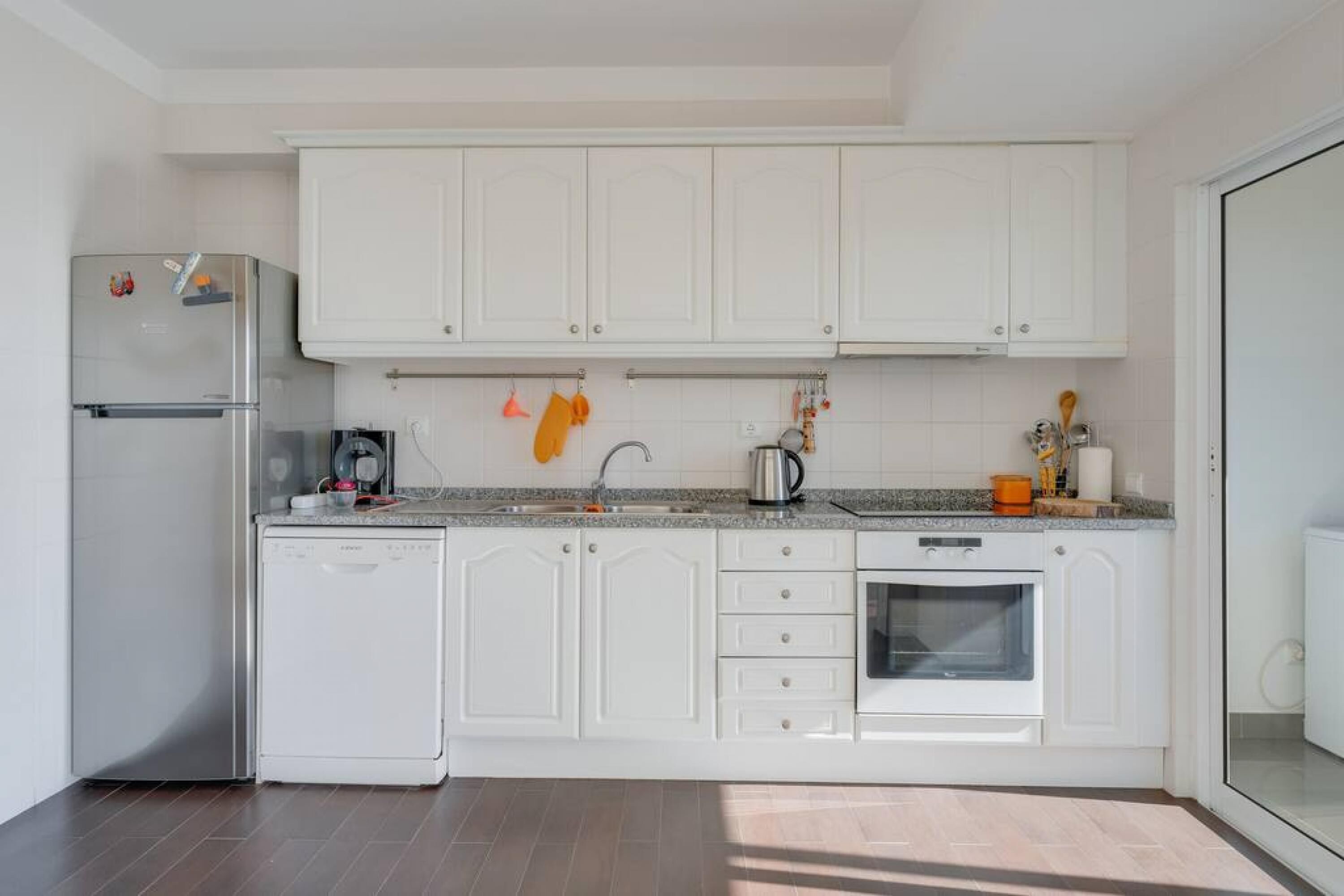 A modern kitchen with white cabinets, a stainless steel refrigerator, a dishwasher, and a built-in oven.