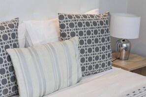 A neatly made bed with patterned pillows and a bedside lamp on a wooden nightstand. - F rum Madeira Ocean View 5B (Funchal)