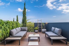 Eine Dachterrasse mit zwei grauen Sofas, einem Holztisch und Topfpflanzen.