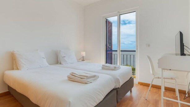 Ein modernes Hotelzimmer mit einem großen Bett, einem Schreibtisch und einem Balkon mit Blick auf die Stadt.