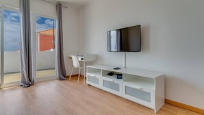 Ein modernes Wohnzimmer mit einem wandmontierten Flachbildfernseher, einem weißen TV-Schrank mit Stauraum, einem weißen Sessel und einer Glasschiebetür, die zu einem Außenbereich führt.