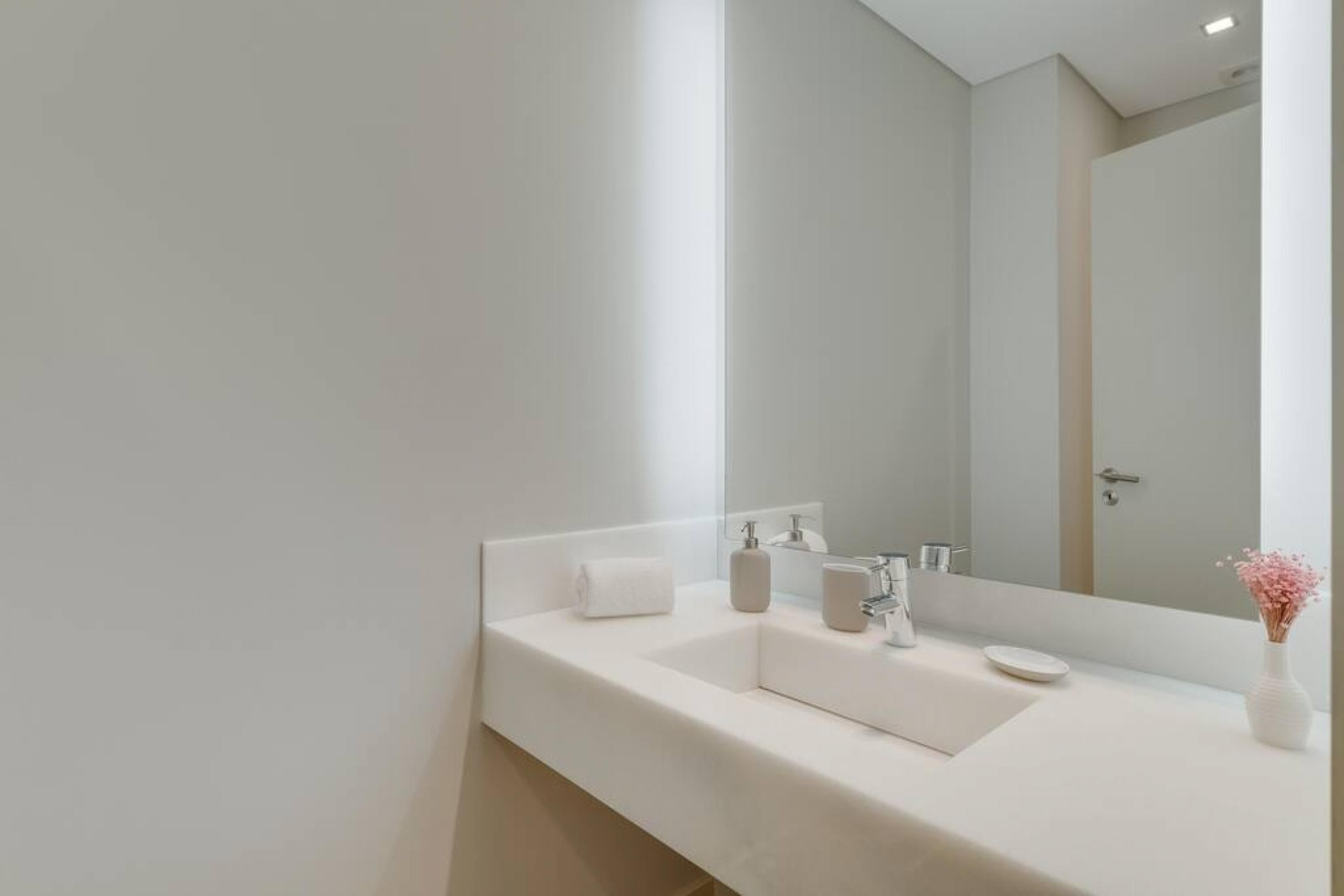A modern bathroom with a white sink, a large mirror, and a vase with flowers.