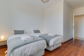 A modern hotel room with two beds, a bedside table with a lamp, and a wooden floor. - Bela S o Tiago I in Funchal (Funchal)