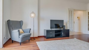 En moderne stue med en grå lænestol, en sort tv-møbel og en gulvlampe.