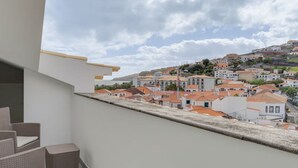 A balcony with wicker furniture, overlooking a town with terracotta-roofed buildings. - Encanto em Santa Cruz (Santa Cruz)