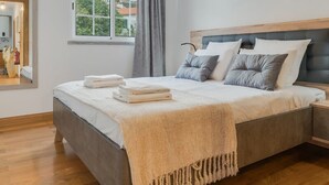 A modern bedroom with a large bed, a bedside table, a mirror, and a window with a view of buildings. - Encanto em Santa Cruz (Santa Cruz)