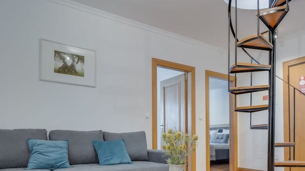 A modern living room with a grey sofa, a wooden coffee table, and a spiral staircase. - Encanto em Santa Cruz (Santa Cruz)
