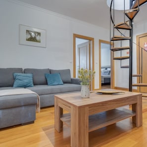 A modern living room with a grey sofa, a wooden coffee table, and a spiral staircase.