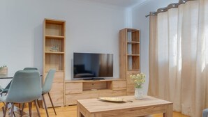 A modern living room with a flat-screen TV, wooden furniture, and a dining area with chairs. - Encanto em Santa Cruz (Santa Cruz)