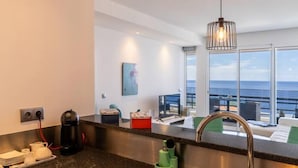 Una cocina moderna con un lavamanos de acero inoxidable, una cafetera y vistas al océano a través de amplios ventanales.