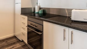 Una cocina compacta con armarios blancos, estufa de acero inoxidable, microondas integrado y un tostador.