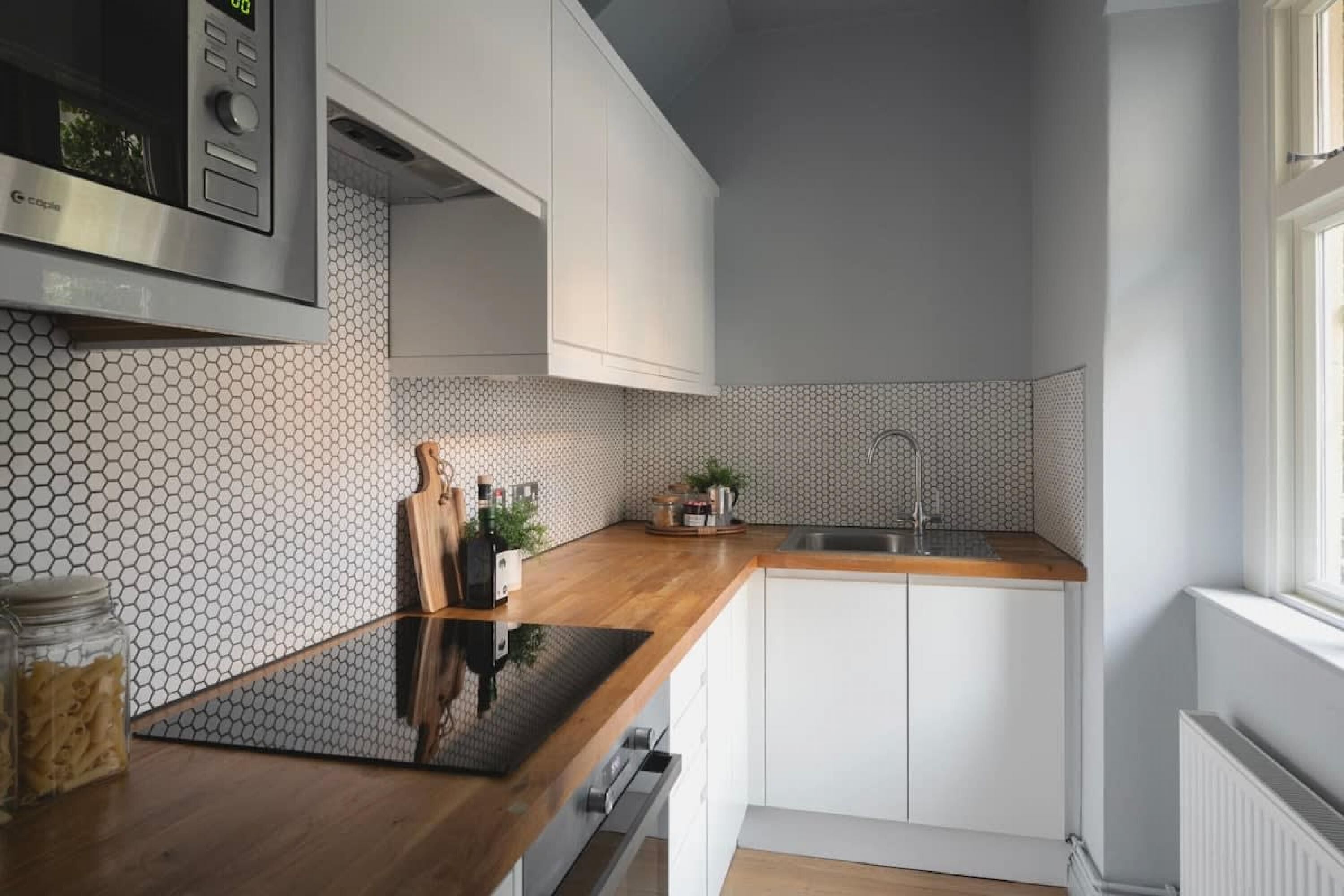 Una cocina moderna con armarios blancos, encimera de madera, microondas de acero inoxidable y un lavamanos.