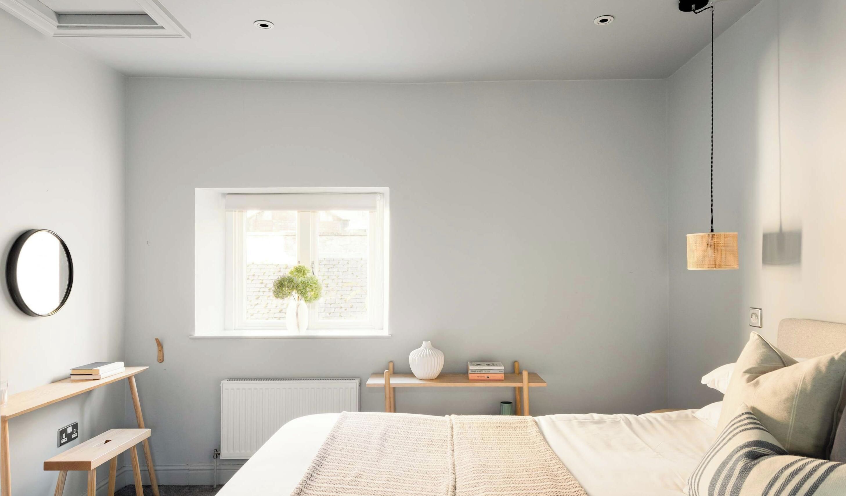 A bedroom with a bed, bedside tables, a window with a plant, and a hanging light fixture.