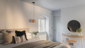 Et moderne soveværelse med en stor seng, et natbord, en hængende lampe og et rundt spejl på væggen.