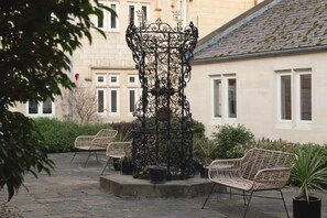 A courtyard with a wrought iron fountain, wicker chairs, and potted plants. - St Catherine s Hospital - Deluxe Apartment (Bath)