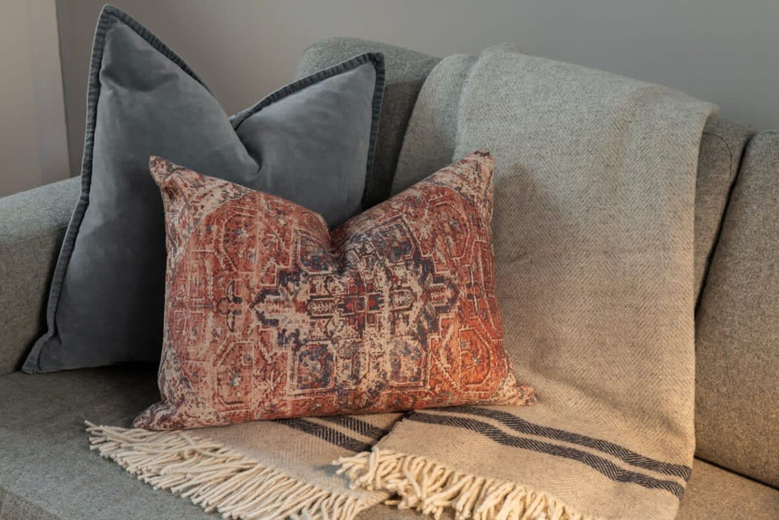A sofa with two pillows, one patterned and one solid grey.