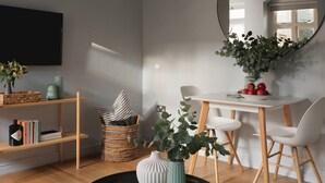 Una sala de estar moderna con un televisor de pantalla plana, estanterías de madera, una mesa de comedor con sillas blancas y un espejo grande.