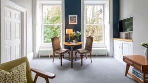 Ein Raum mit zwei weißen Doppeltüren, einem runden Tisch mit Stühlen, einer Lampe und einem Gemälde an der Wand.