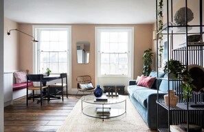 A living room with a sofa, a coffee table, a dining table with chairs, and two windows. - Luxurious Apartment - Minutes From Angel Tube St (London)