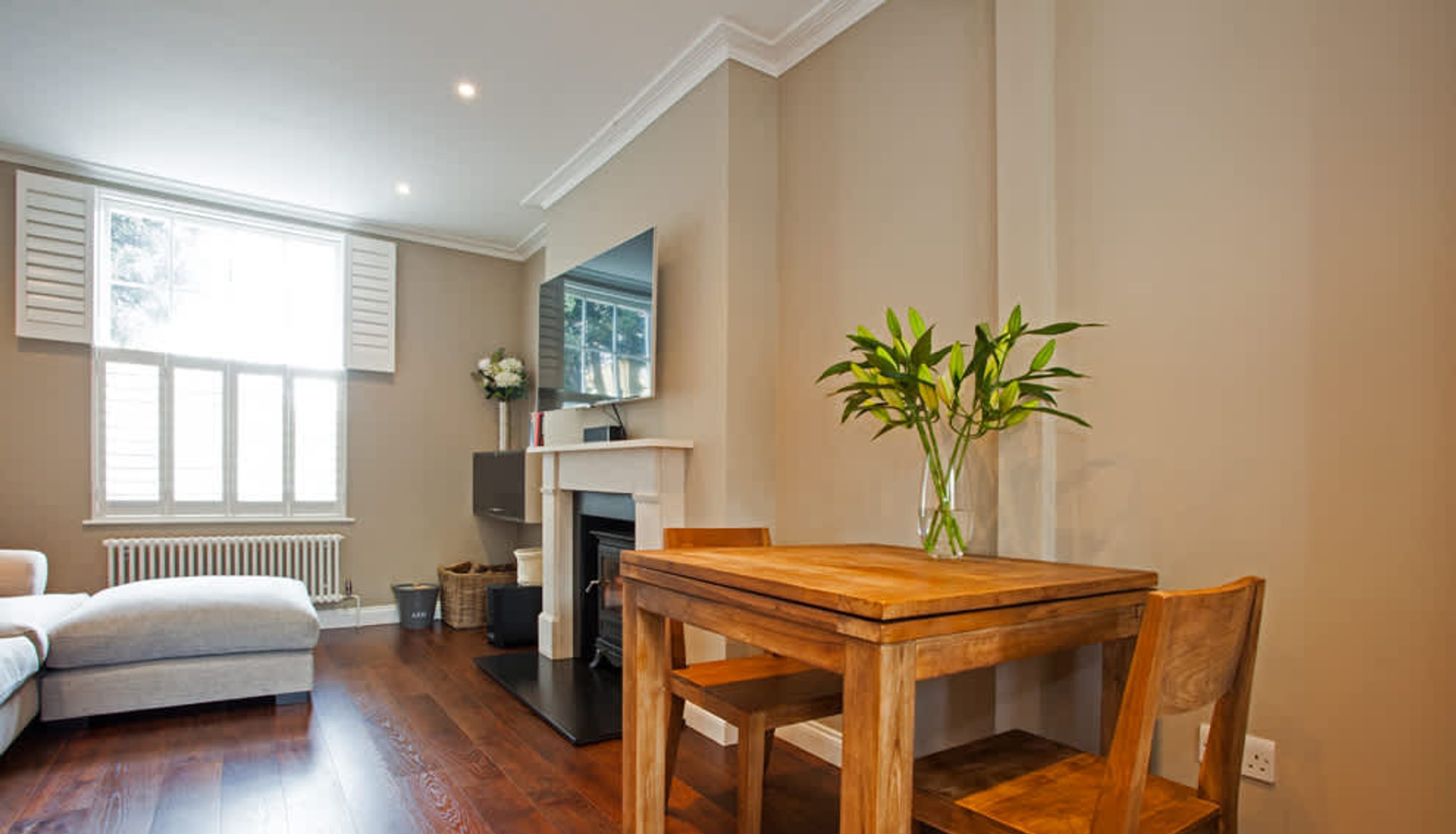 A living room with a wooden dining table, a sofa, a fireplace, and a TV mounted on the wall.