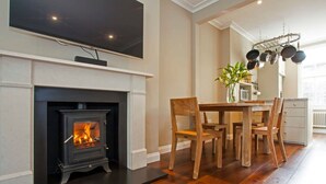 A living room with a fireplace, a dining table with chairs, and a TV mounted above the fireplace. - Luxury Marylebone House With Private Garden (London)