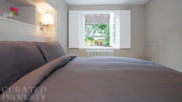 A bedroom with a bed, a window with open shutters, and a radiator below. - Luxury Marylebone House With Private Garden (London)