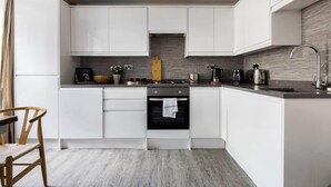 A modern kitchen with white cabinets, a central island, a stove, and a sink. - Modern Duplex Near Oxford Street (London)