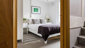 A bedroom with a bed, bedside tables, a framed picture on the wall, and a striped rug. - Modern Duplex Near Oxford Street (London)