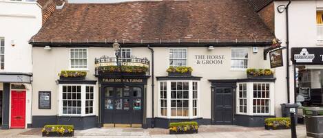 A traditional pub with a black and white facade, named 'The Horse & Groom'. It features a black door with a sign above it, and flower boxes on the ground floor.