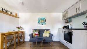 A cozy living area with a sofa, a coffee table, and a rug. There is a kitchen area with cabinets and a microwave. - Lavender Folly - Cosy Accommodation Alresford (Alresford)