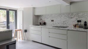 A modern kitchen with a marble backsplash, white cabinetry, a sink, and a stool. - Stylish Georgian Townhouse w Sun Terrace Garden (London)