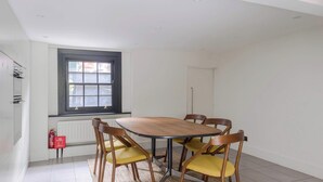 A dining area with a table and four chairs, a window with blinds, a radiator, and a fire extinguisher. - Stylish Georgian Townhouse w Sun Terrace Garden (London)