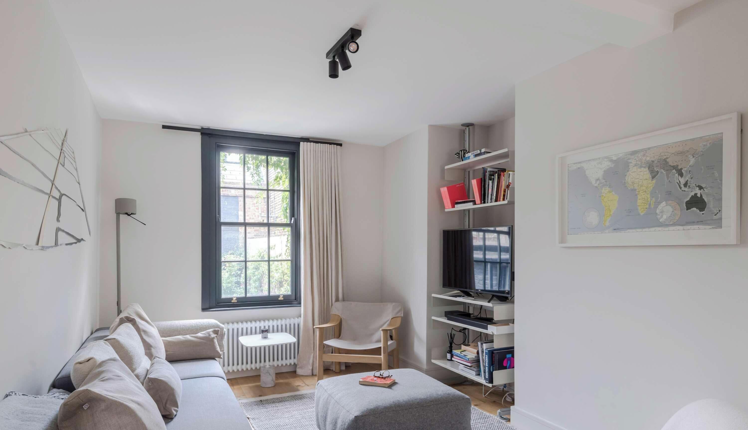 A modern living room with a sofa, a chair, a TV, a bookshelf, and a window with curtains.