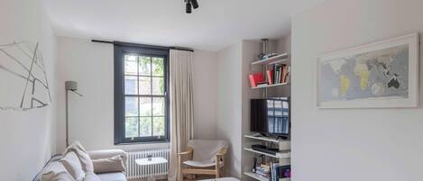 A modern living room with a sofa, a chair, a TV, a bookshelf, and a window with curtains.
