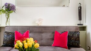 Un salon moderne avec un canapé gris, deux coussins rouges, un vase avec des fleurs jaunes et un objet décoratif accroché au mur.