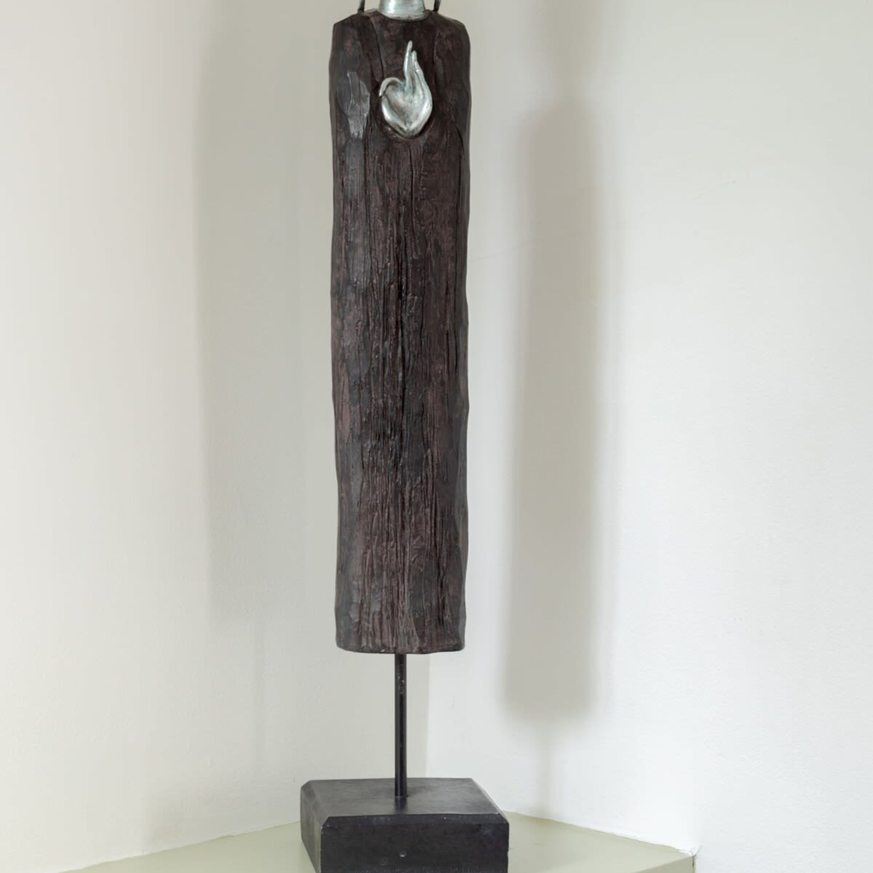 A tall, dark wooden sculpture with a metallic figure at the top, mounted on a black base.
