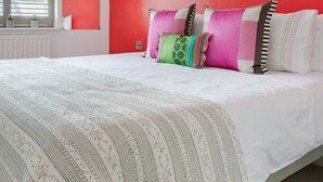 Une chambre avec un mur d’accent rouge, un lit blanc et plusieurs coussins colorés.