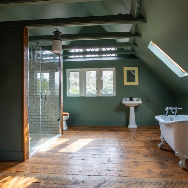 A spacious bathroom with a wooden floor, a glass shower enclosure, a white sink, and a clawfoot bathtub. - Large Country House in Ashdown Forest (East Grinstead)