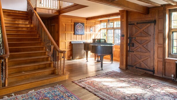 A grand wooden interior with a staircase, a grand piano, and a large rug. - Large Country House in Ashdown Forest (East Grinstead)